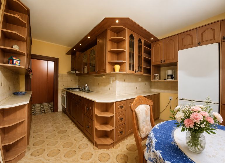 The kitchen of a 4-room apartment with a wooden decor, flowers on the table, cabinets, and appliances.