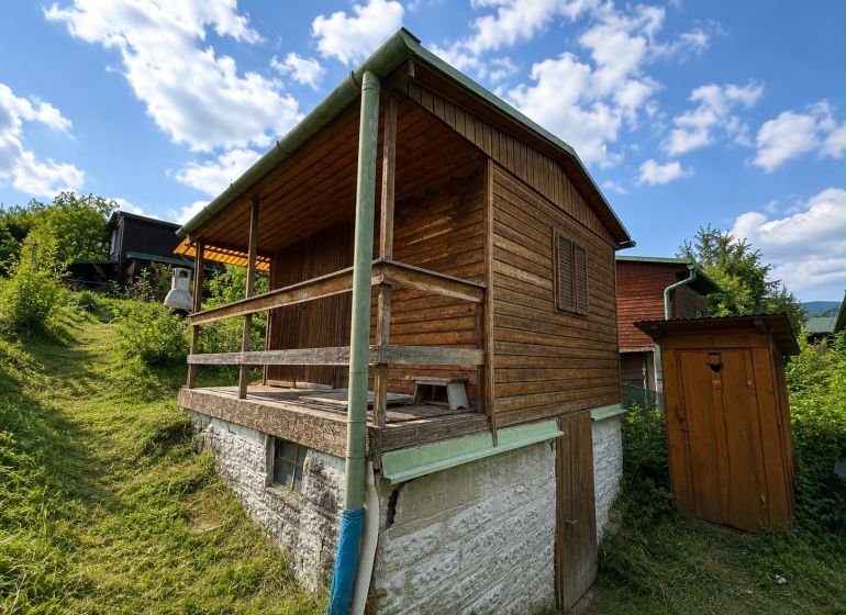 A wooden cottage in Žilina surrounded by greenery and blue sky.