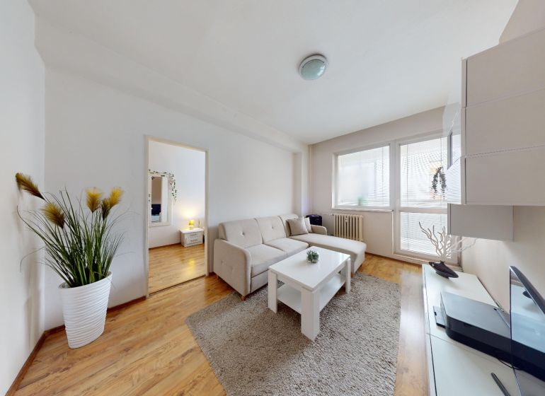 Living room in a two-room apartment on K výstavisku street with a comfortable sofa and wooden floor.