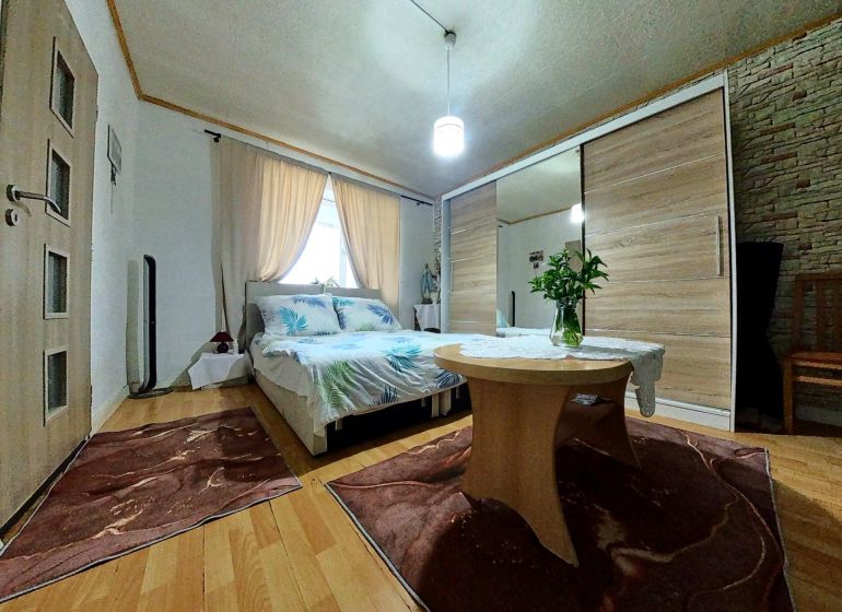 A bedroom in a family house with a wooden decor floor, flowers on the table, and a bed.