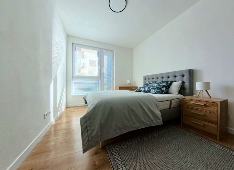 A bedroom in a 3-room apartment with a wood-patterned floor and a large window.