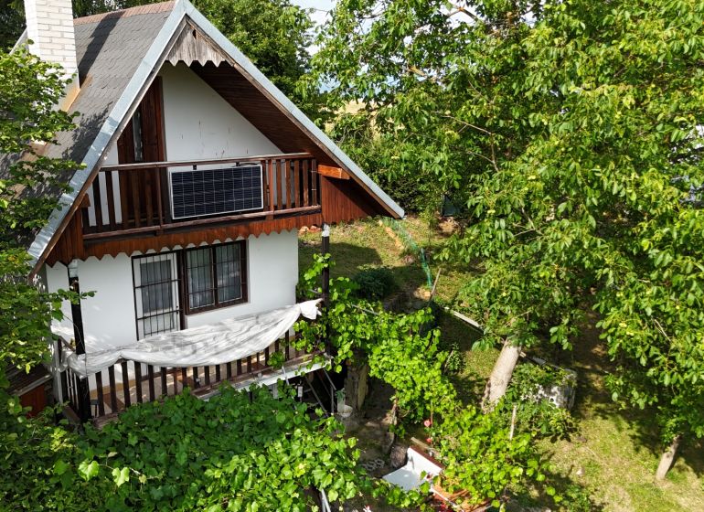 A cottage in Banská Bystrica surrounded by greenery with a wooden balcony and a photovoltaic panel.