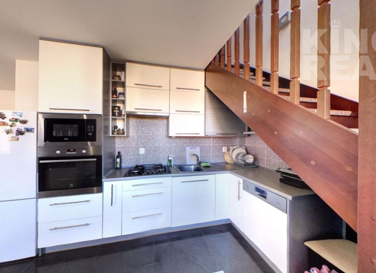 A kitchen in a 2-room apartment with stairs and appliances, with a wooden decor floor.
