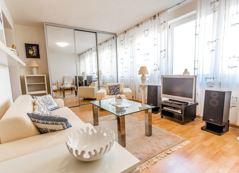 A bright living room with a cream sofa, a glass table, and a wooden decor floor.