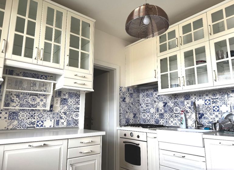 A kitchen unit with glass cabinets and blue-white tiles in a 3-room apartment.