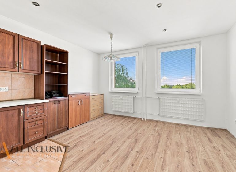 A kitchen in a 2-room apartment with a wooden decor floor, cabinets, and windows.