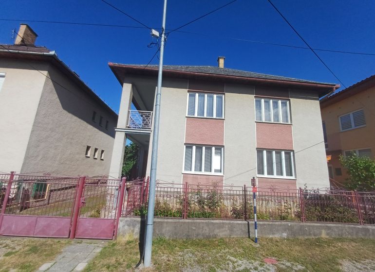 A family house in Rožňava with a brick fence, located between two other houses.