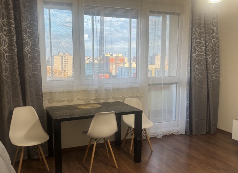 Dining area with a table, white chairs, and a floor with a wooden decor in a 3-room apartment.