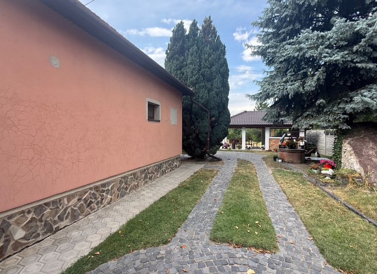 A family house in Iža with a stone exterior cladding, trees, and a landscaped garden.