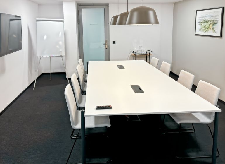 Conference room with a long table, chairs, flipchart, and modern lighting.