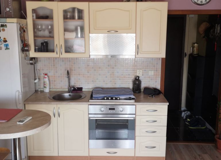 A kitchen in a studio apartment with a kitchen unit, wood decor, and appliances.