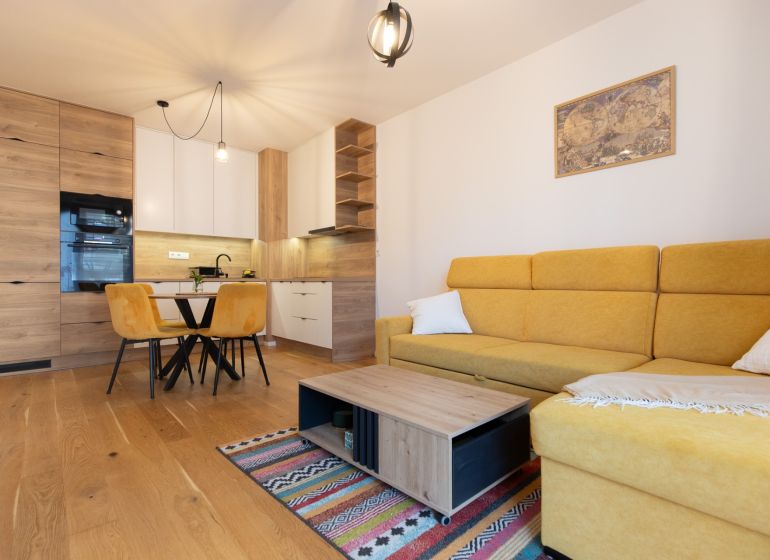 2-room apartment with wood-patterned flooring, yellow sofa, dining table, and kitchen.