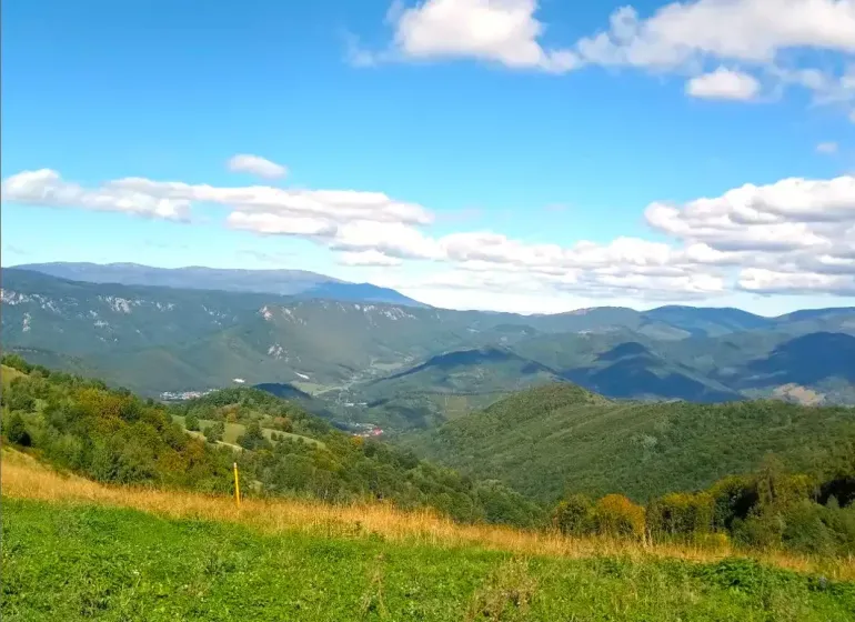 Hilly landscape of agricultural and forest land in Ratkovské Bystré under a blue sky.