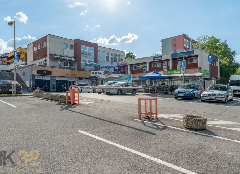 A parking lot with shops and a restaurant in Banská Bystrica, with cars parked around.