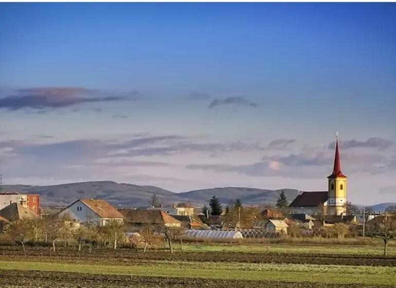 A village with a church in Kamenný Most surrounded by agricultural and forest lands.