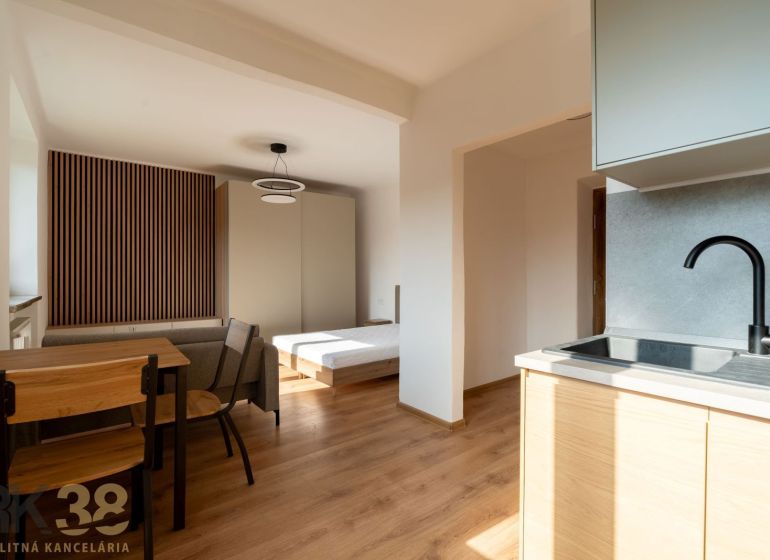 A kitchen with a kitchen unit, a dining table, and a bed, with a wooden decor floor.