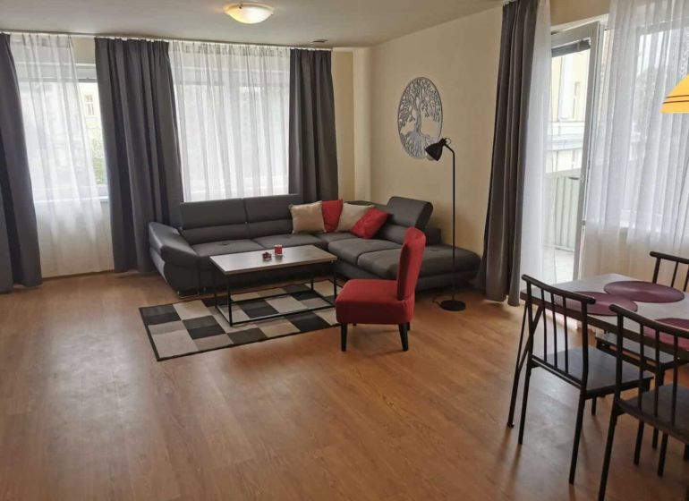 Living room in a family house with wood-patterned flooring, a gray sofa, and a dining table.
