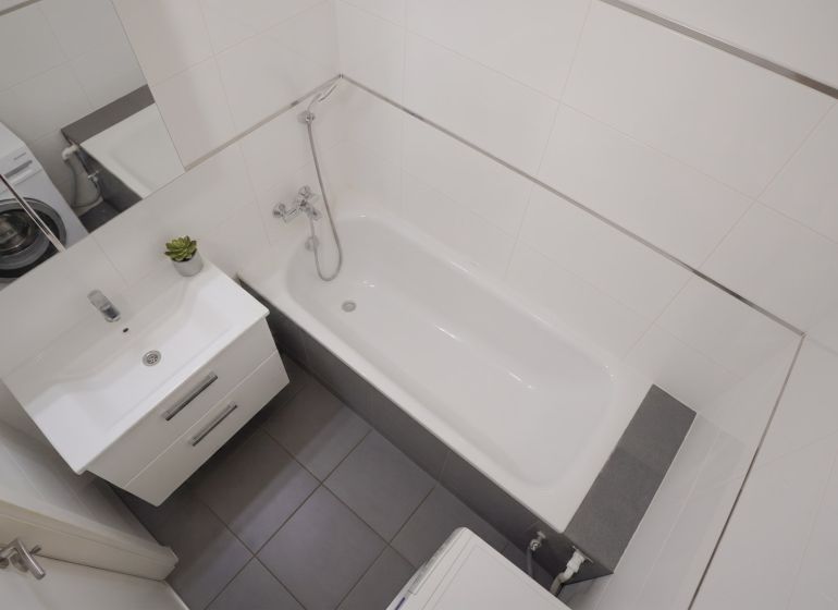 A bathroom with a bathtub, washing machine, sink, and white tiles in a 3-room apartment.