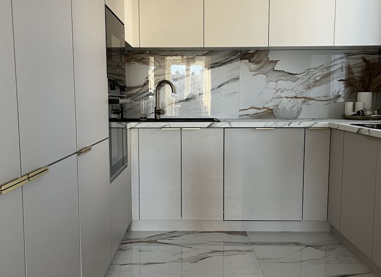 A kitchen in a 2-room apartment with white cabinets and marble tiles.