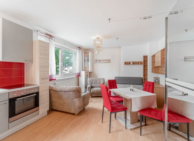 A kitchen with a dining table and a sofa in a studio apartment, floor with wood decor.