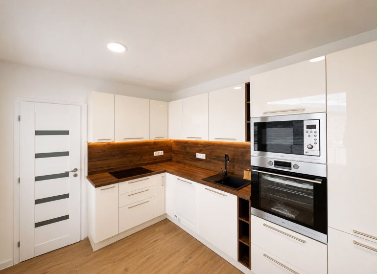 Bright kitchen in a 2-room apartment with wood-patterned flooring and built-in appliances.