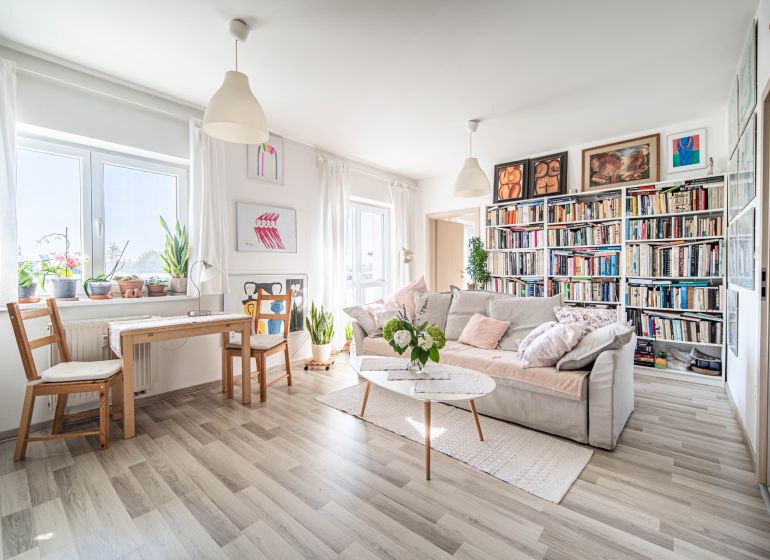 Living room in a two-room apartment with a wooden decor floor, a bookshelf, and a sofa.
