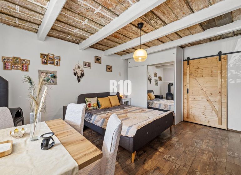 Interior of a family house with a bed, dining table, and decorative wooden ceiling.