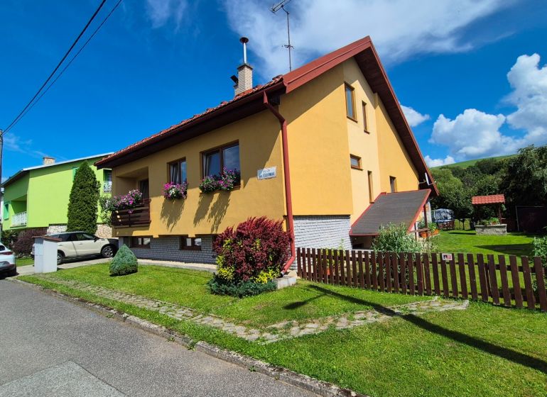 A family house in Podolínec with a garden and a yellow facade, surrounded by greenery.