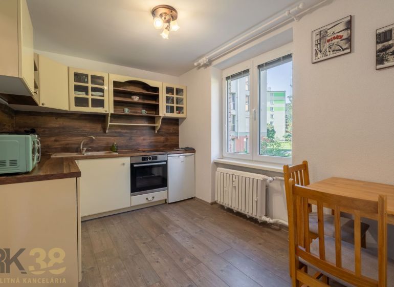 A kitchen in a studio apartment with a wood-patterned floor, light cabinets, large window.