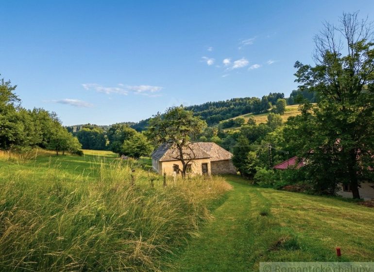 A family house in Dobroč surrounded by nature and green meadows under a blue sky.