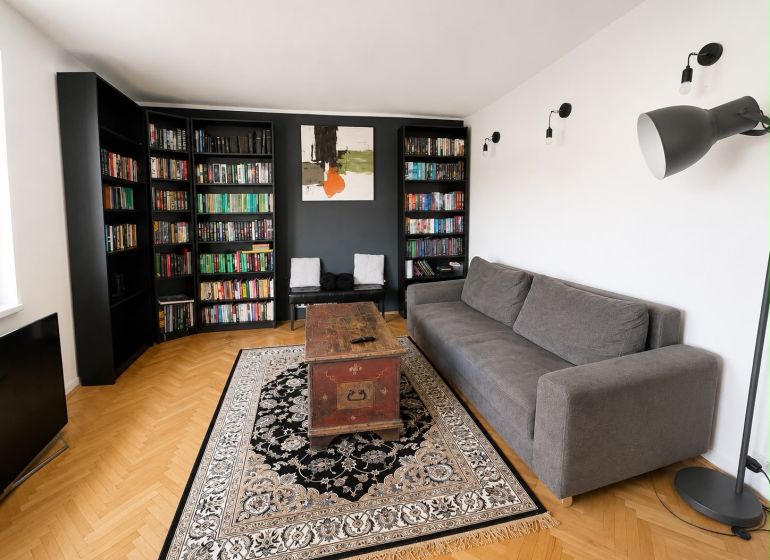 Living room with a bookshelf and a gray sofa in a 3-room apartment, floor with wood decor.