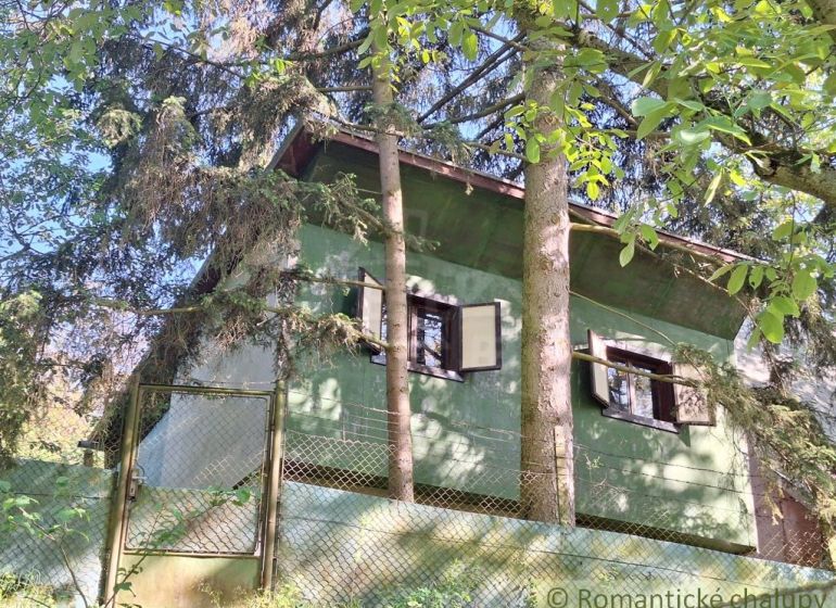A cottage surrounded by trees in Kamenica nad Hronom, green facade, closed shutters.