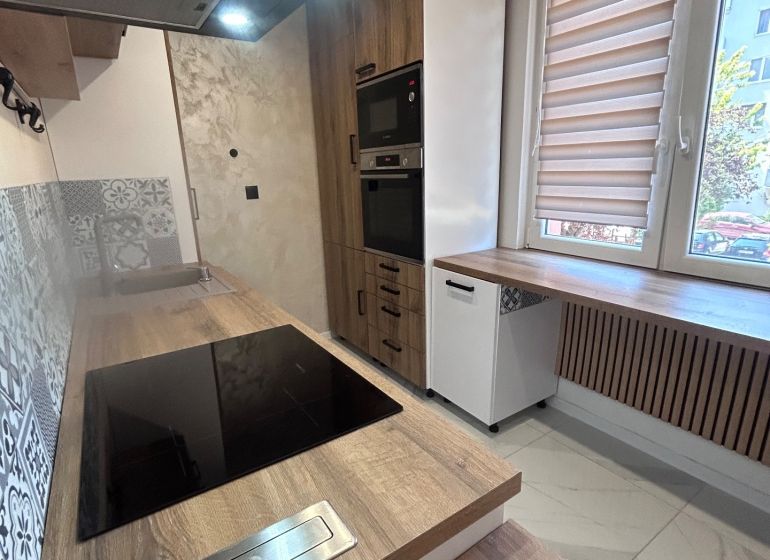 A kitchen with built-in appliances and a wooden decor floor in a 3-room apartment.