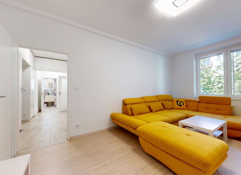 A living room with a striking yellow sofa and a wooden-patterned floor in a two-room apartment.