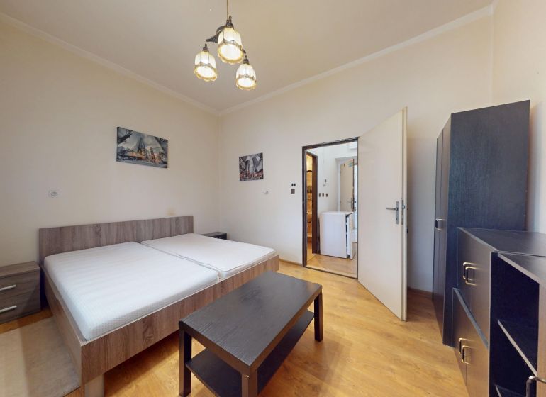 A bright bedroom with a bed, wardrobe, and wooden decor flooring in a studio apartment.