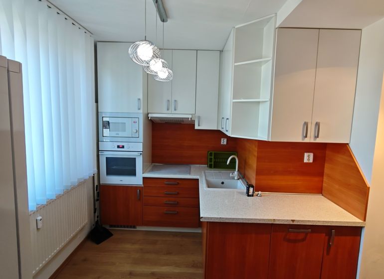 A kitchen in a studio apartment with built-in appliances and a wooden decor floor.