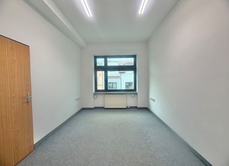 Office with white walls, carpeted floor, window, and wooden door.