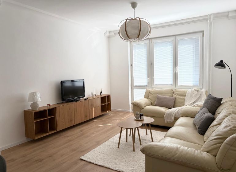 A bright living room of a 3-room apartment with sofas, a TV, and a wooden-decor floor.