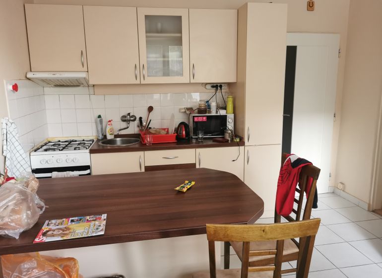 A kitchen in a studio apartment with a stove, wooden decor, and white cabinets.