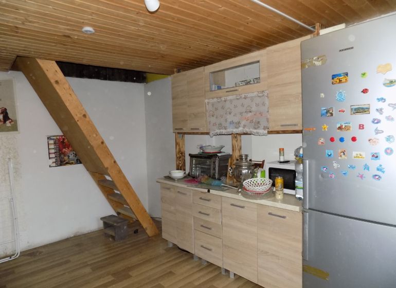 Interior of a cabin with a wooden ceiling, kitchen counter, and staircase, floor with wooden decor.