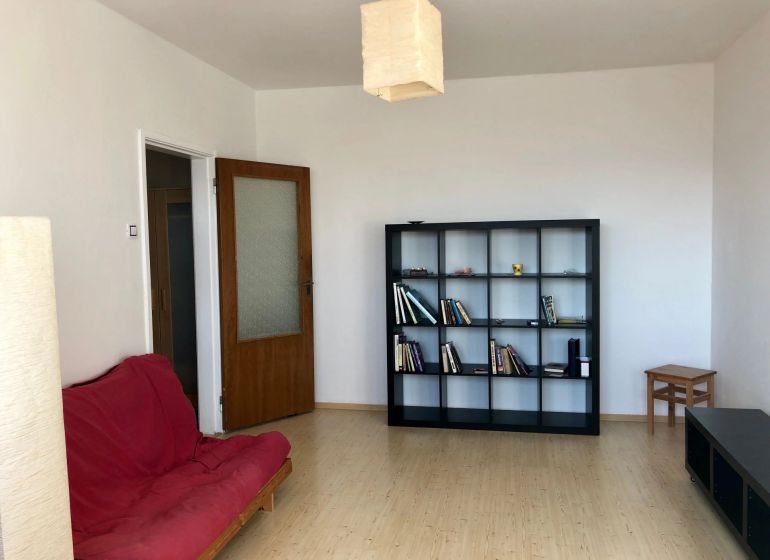 A room in a one-room apartment with a shelving system, a red sofa, and a wooden decor floor.