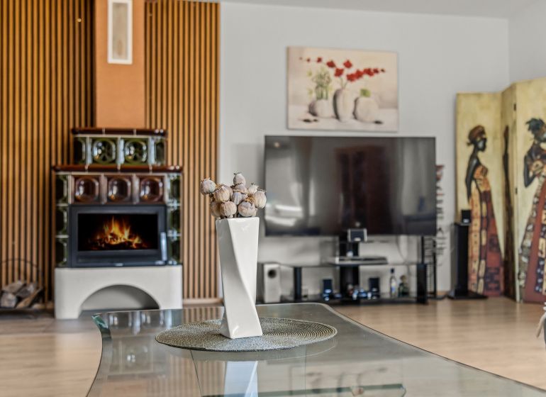 A family house with a tiled stove and a decorative vase on a glass table.