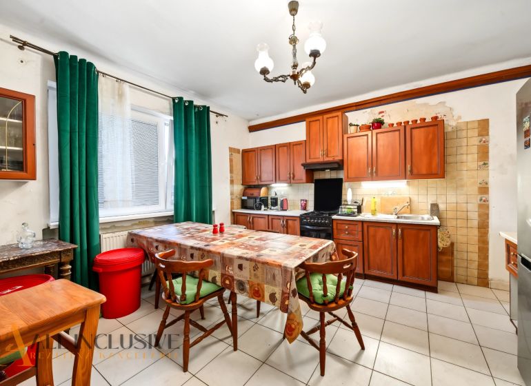 A kitchen in a family house with wooden cabinets, a dining table, and green curtains.