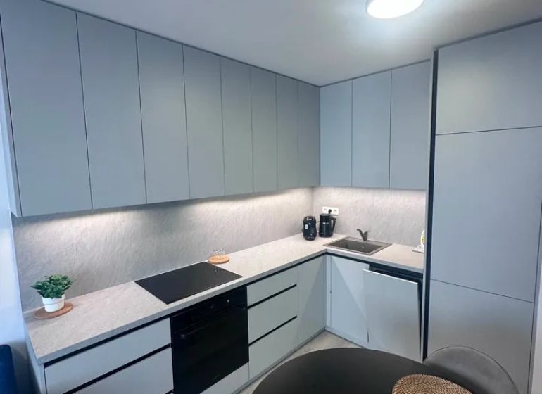 A kitchen in a 2-room apartment with a wooden decor floor and gray cabinets.
