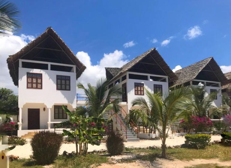 A family house in Fumba Town with palm trees and a thatched roof under a blue sky.