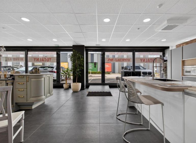 Interior of commercial space with a kitchen counter, bar stools, and large glass doors.