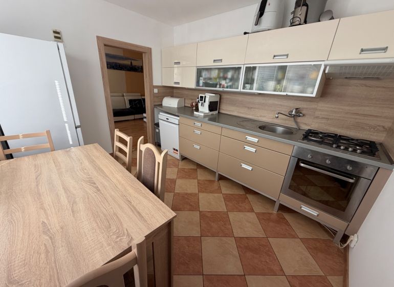 A kitchen of a 3-room apartment with a corner unit, dining table, and appliances.