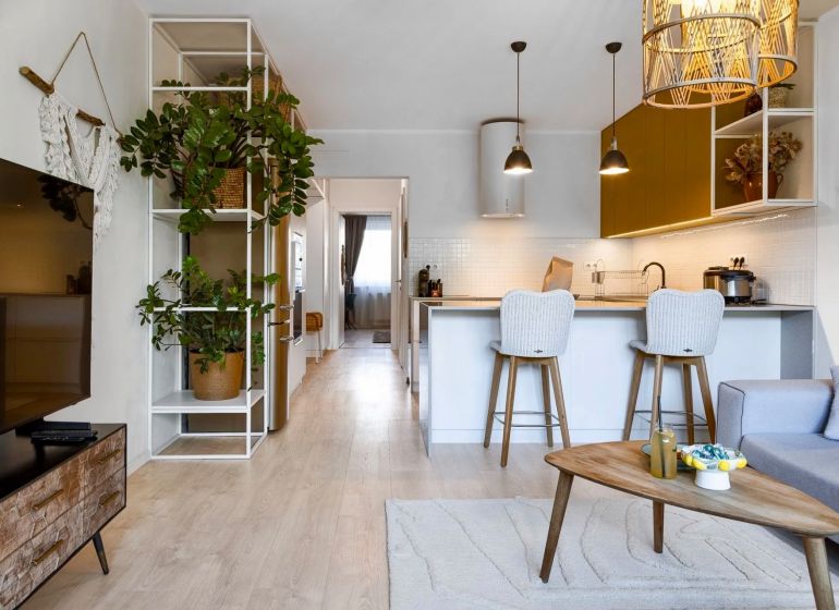 Interior of a 2-room apartment with a kitchen counter, wooden decor flooring, and greenery.