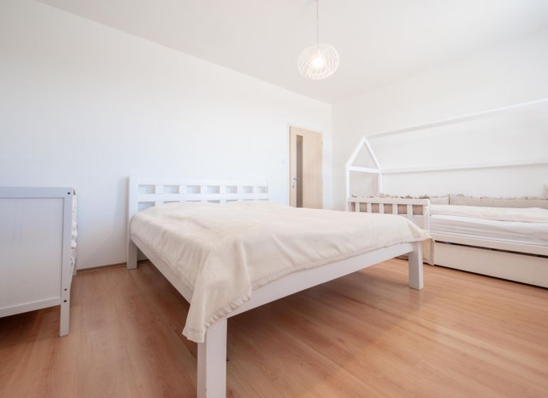 A bedroom with wood-patterned flooring, a double bed, and a child's bed.