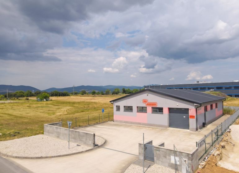 An industrial building in Nová Dubnica surrounded by fields and mountains.